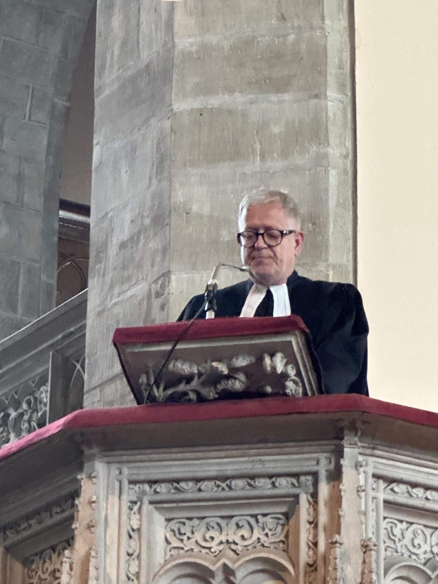 Ein Mann mit einem schwarzen Talar steht auf der Kanzel und spricht in ein Mikrofon.
