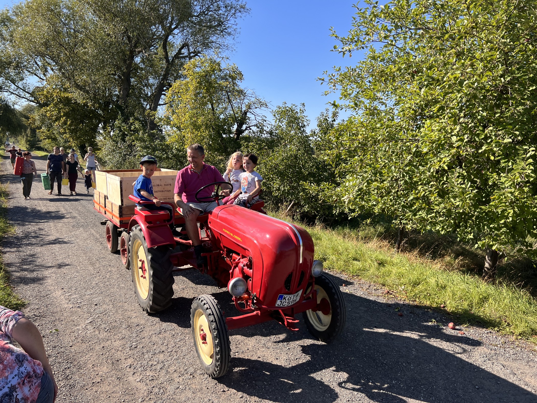 Kinder und ein Erwachsener fahren auf einem roten Traktor und ziehen dabei einen Anhänger mit Äpfeln