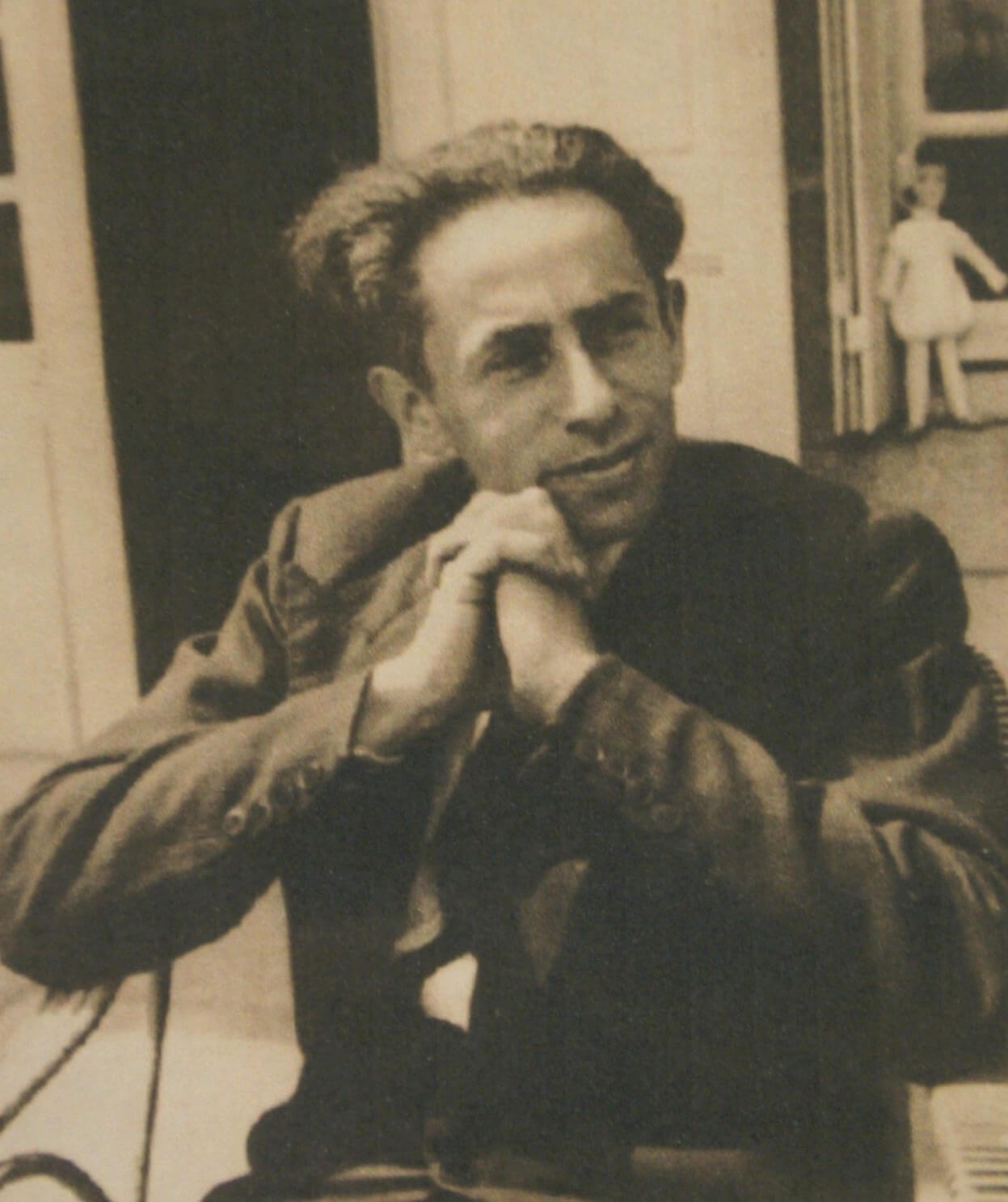 Ein Foto eines jungen Mannes, der mit locker gefaltenen Händen auf einem Stuhl sitzt.^