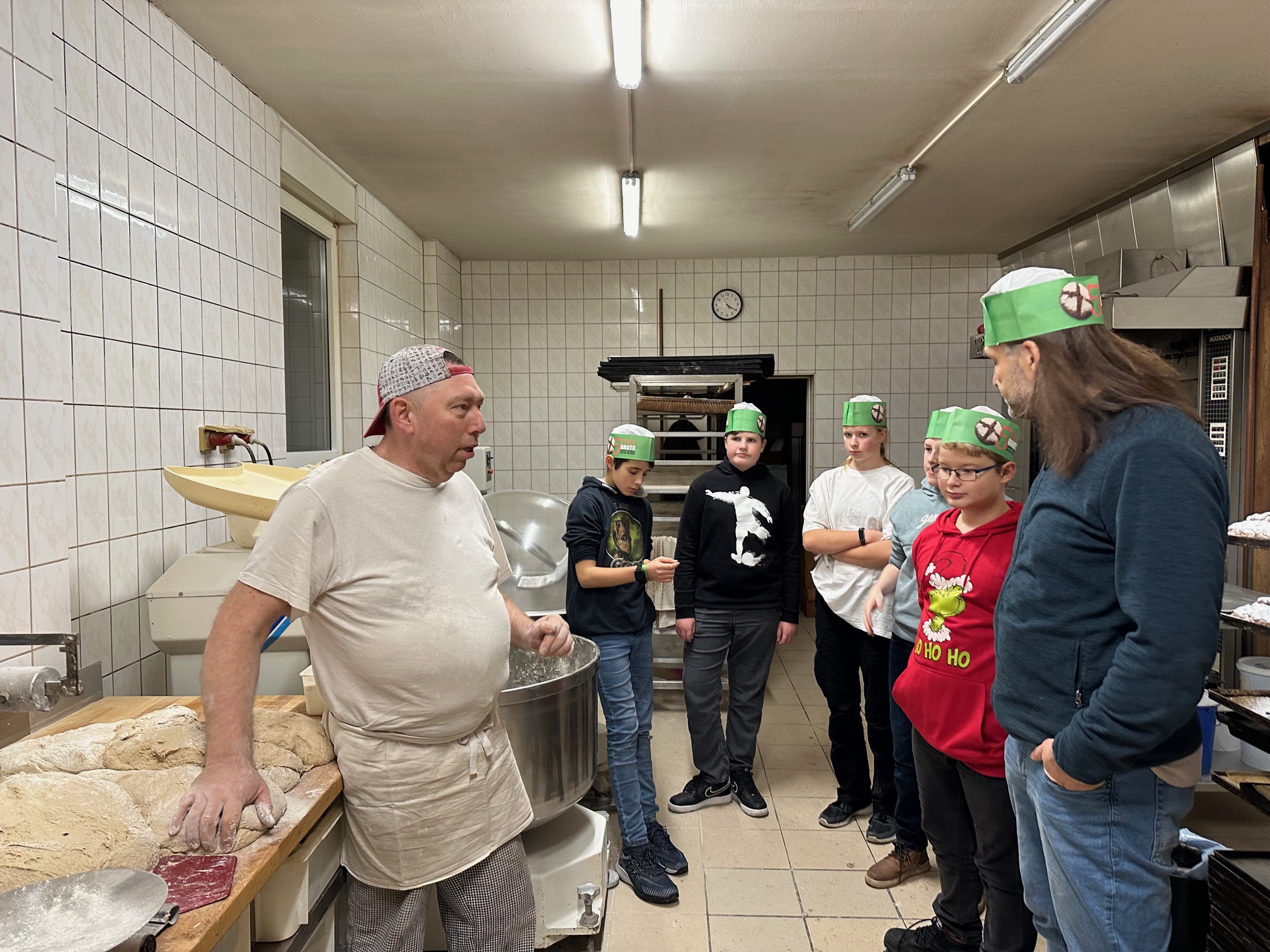 Bäckermeister erklärt Jugendlichen in der Backstube die Brotherstellung