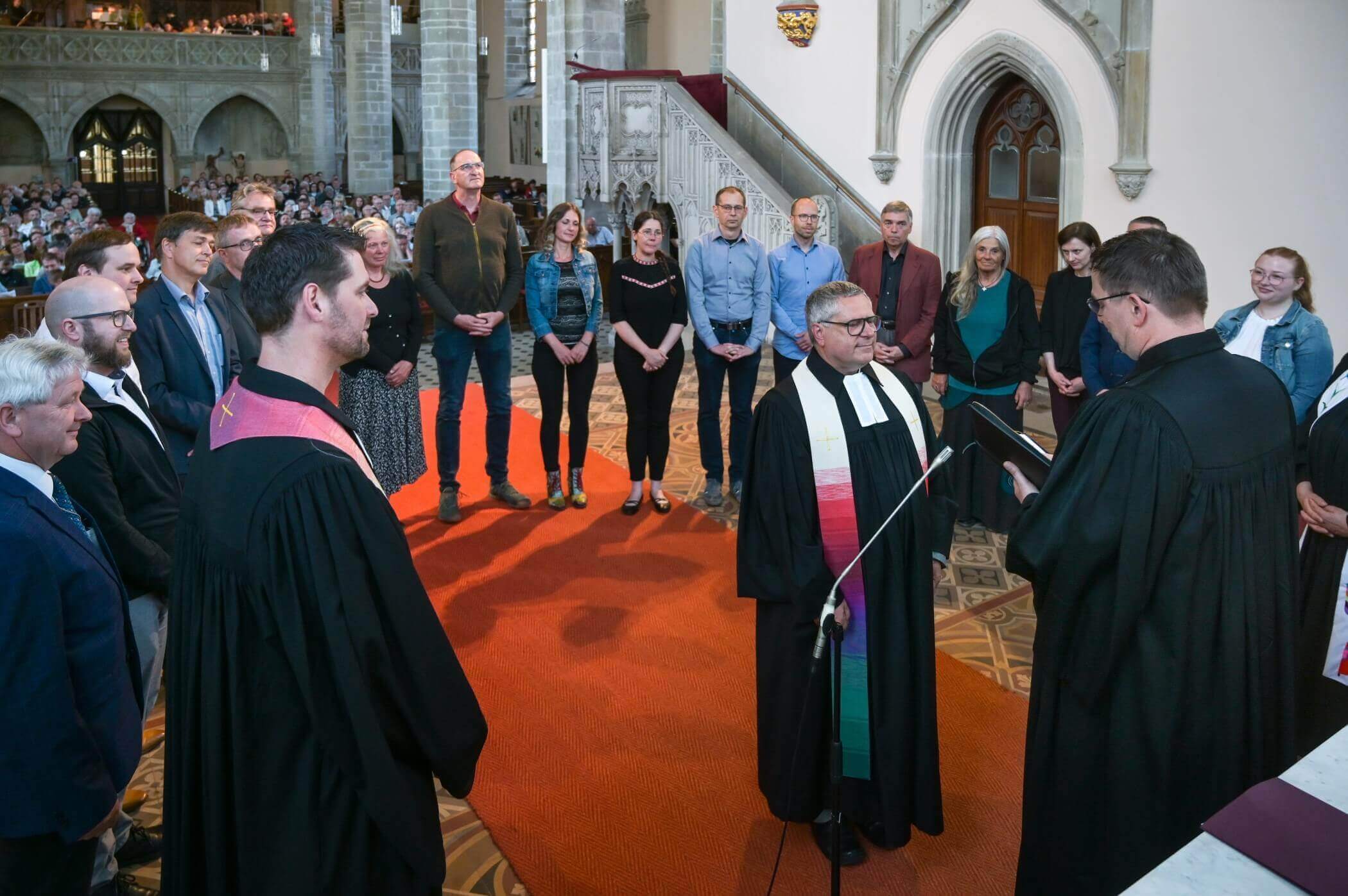 Menschen stehen im Altarraum im Kreis um einen Pfarrer herum im Hintergrund ist die vollbesetzte Kirche zu sehen