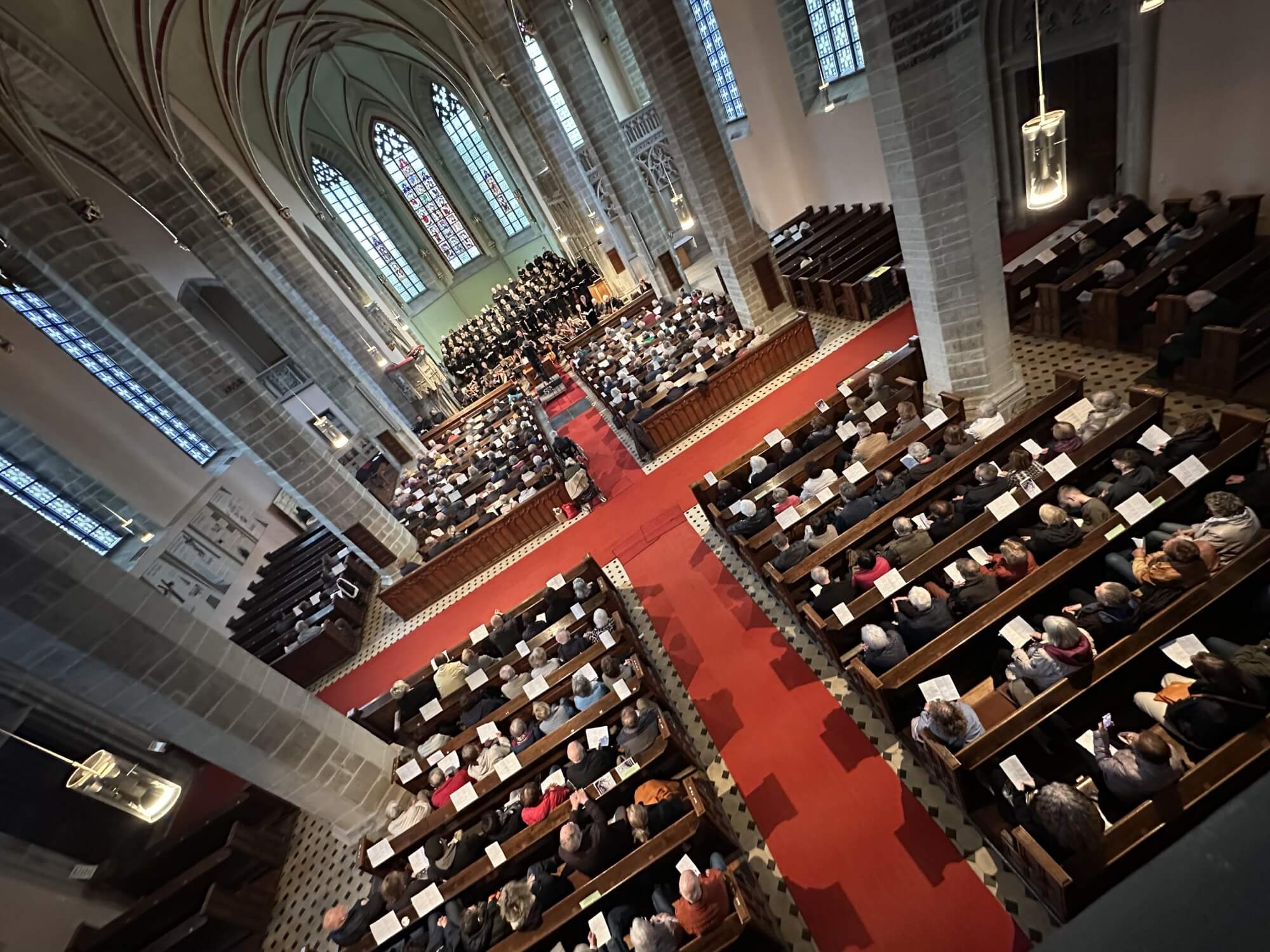 Blick von oben in eine gut gefüllte Kirche. Vorn im Altarraum steht ein Chor in schwarzer Kleidung. Davor sitzt ein Orchester. 
