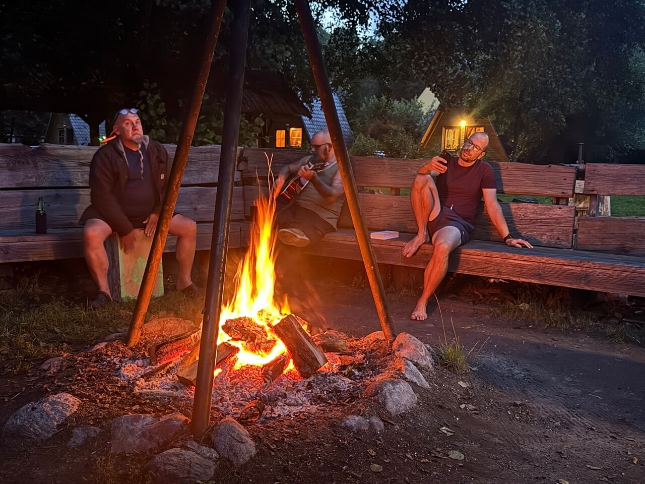 drei Menschen sitzen am Lagerfeuer und machen Musik mit Cachon, Gitarre und Gesang