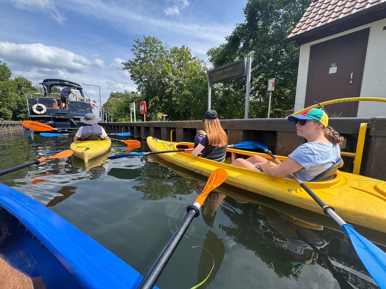 Menschen in blauen und gelben Kajaks warten in einer Schleuse auf die Schleusung