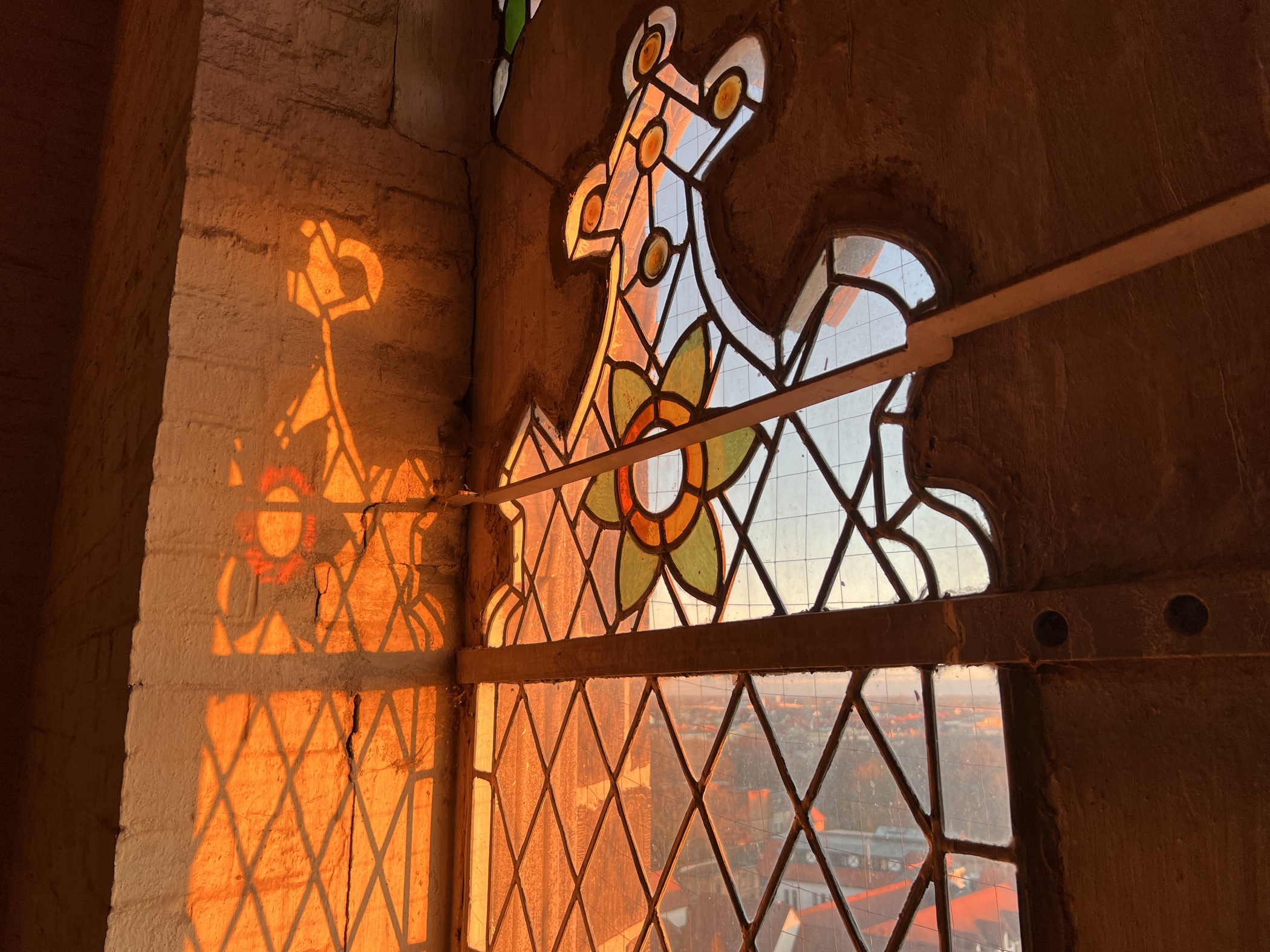 Ein Kirchenfenster durch das die Sonne scheint mit dem Lichtspiel dazu an der Wand