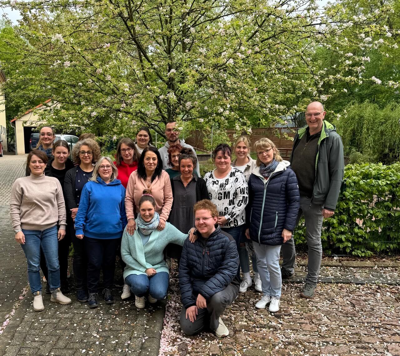 Alle Mitarbeiterinnen und Mitarbeiter der KiTa vor einem blühenden Kirschbaum im Hof der Einrichtung